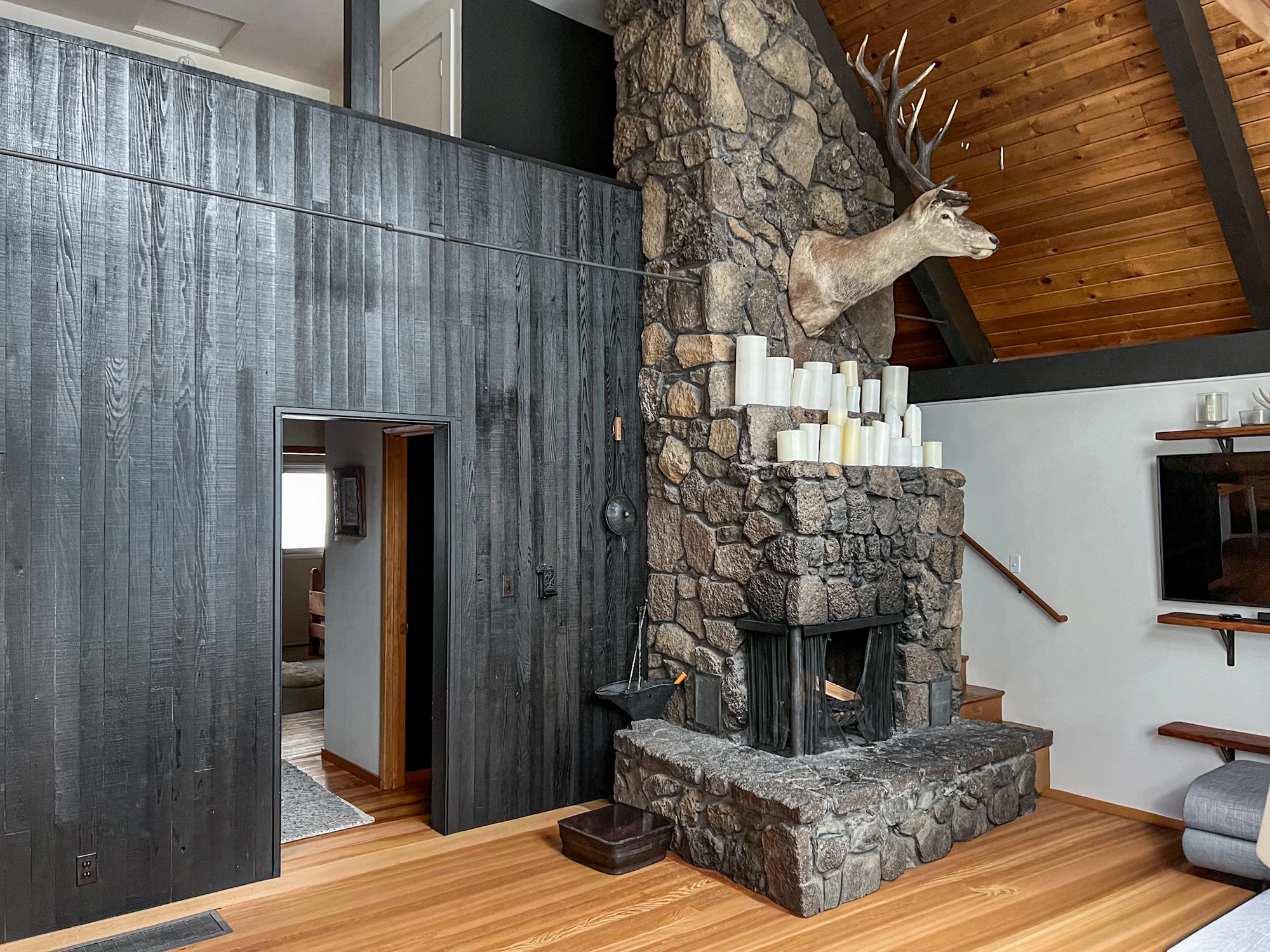 Tungsten Lodge, three-story lava rock chimney with mounted stag, candle mantel and blackened shou-sugi-ban wall against Douglas Fir ceilings